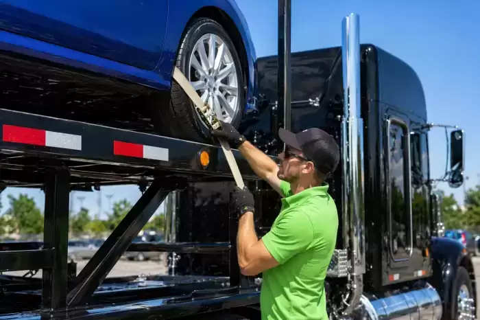 photo of auto transport driver strapping down vehicle on a trailer